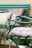 Verschieden gemusterte Kissen auf türkisfarbener Bank und einem Gartenstuhl im alten, französischen Landhausstil
