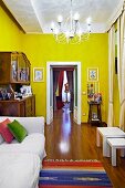 White sofa next to antique dresser and open double doors in yellow-painted interior