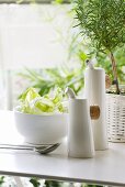 Porcelain vinegar and oil bottles next to salad bowl and rosemary plant