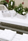 Geschirr und Topfblume in Rattankörben auf einem weissen Gartentisch mit passender Sitzbank