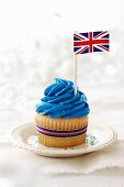 A vanilla cupcake topped with blue frosting and a British flag