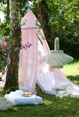 Mattress under canopy, floor cushions and bamboo lanterns in garden