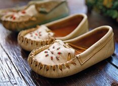 White children's moccasins with bead work on a dark wooden floor