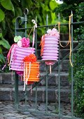 Mit Dekobändern, Papierblumen und Papierstreifen dekorierte Zuglaternen hängen am Gartentor