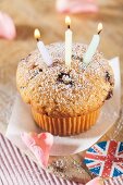 A cupcake with three candles with Union Jack decorations and rose petals next to it