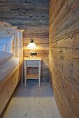 Bedside table with lit lamp in bedroom of wooden hut