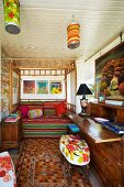 Sleeping and work areas in simple bedroom - bamboo four poster bed with colourful striped cover and upholstered stool in foreground at antique bureau