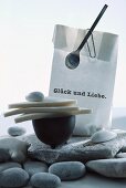 Decorations for summer party on river bank: pebbles, triangles of bread and pebble on dish, paper bag with printed congratulations, paper clip and spoon