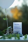 Menu card for summer party on river bank; stacked pebbles, balloon and fennel fronds as table decoration