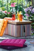 Gelbvioletter Farbklang für den Drink im Sommergarten - gestreifte Kühlbox und Sitzkissen vor blühendem Oleander und Phloxs