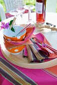 Spotty bowls, colourful fabric place mats and striped cutlery on wooden tray in garden