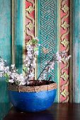 Flowering twigs in blue pot against painted and carved wooden wall