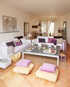 Cushions in shades of purple on white sofas in bright, open-plan living-dining room with terracotta floor