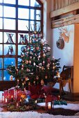 Geschmückter Weihnachtsbaum mit brennenden Kerzen in Zimmerecke vor raumhohem Fenster mit Sprosseneinteilung