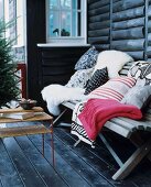Sheepskins, cushions and blankets on wooden bench on terrace