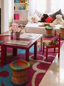 Colourful children's table and chairs; soft toys and cushions on bed in background