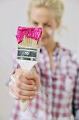Renovierungsarbeiten - Frau hält einen in Farbe eingetauchten Pinsel in der Hand