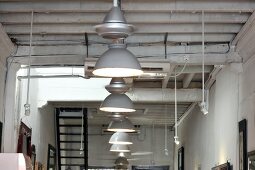 Row of pendant lamps with metal lampshades hanging from simple wooden ceiling in restaurant interior