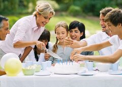 Outdoor birthday party, mature woman cutting birthday cake