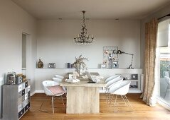 Moderner Holztisch und weiße Schalenstühle unter Deckenkerzenleuchter in schlichtem Wohnzimmer