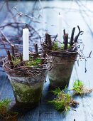 Arrangements of moss, twigs and candles in vintage plant pots on wooden surface