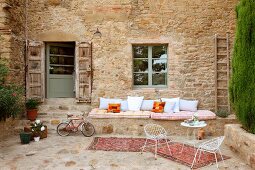 Courtyard with delicate terrace chairs and table in front of masonry bench on outside wall of Italian farmhouse