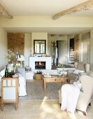 Simple interior in pale shades with wingback chairs and coffee table in front of open fire in Mediterranean country house