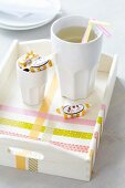 Becher mit Strohhalmen und Karamellbonbons auf Tablett mit Masking Tape Deko