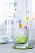 Candles decorated with stripes of tape in drinking glass filled with decorative pebbles