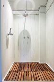 Simple shower area with white wooden walls and wooden slats on floor