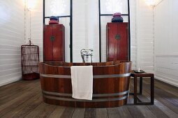 Free-standing wooden bathtub in front of delicate, Oriental-style cabinets against white wall