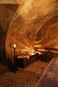 Dramatisches Lichtspiel von kugelförmiger Tischlampe auf Gewölbedecke in rustikalem Schlafzimmer mit altem Kieselsteinboden