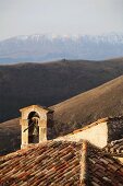Ziegeldach einer alten italienischen Kirche mit Glockenturm und Blick in die Gebirgslandschaft