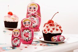 Russian dolls and a cupcake decorated with cherries and heart-shaped sprinkles
