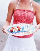 A woman serving mozzarella and tomato on sticks with grissini for a picnic