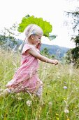 Little blond girl running with a rhubarb leaf through a field