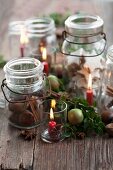 Einmachgläser mit Zimtsternen, Maroni und Zimtstangen zwischen Kerzen in kleinen Gläsern