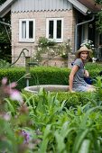 Frau sitzt am Brunnen im Garten