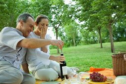 Mature couple having picnic outdoors, opening bottle of wine