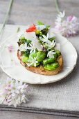 A slice of bread topped with broad beans, herbs and edible flowers
