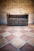 Schnitzereien an antiker, rustikaler Holzbank in puristischem Raum mit Terrakotta-Fliesen und Ziegelwand
