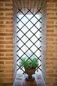 Vergitterte Fensteröffnung mit kleiner, bepflanzter Amphore in Ziegelmauerwerk