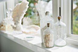 Verschieden grosse, gefüllte Glasflaschen mit Korkverschluss auf Fensterbank
