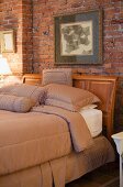 Elegantes Bett mit Kopfteil aus geschnitztem Holz vor rustikaler Ziegelwand