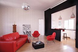 Minimalistisches Wohnzimmer mit roter Lack Couch und roten Sesseln vor offener Küche mit schwarzem Raumteiler