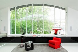 Red armchair and black side table in minimalist interior with huge window