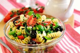 A bowl of pasta salad with green beans, peas, tomatoes, olives and spring onions