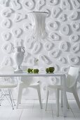 White dining table and white chairs in front of wall decorated with loop-shaped elements