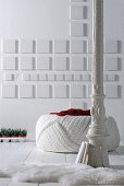 White, vintage metal column in front of pouffe and white square elements on wall
