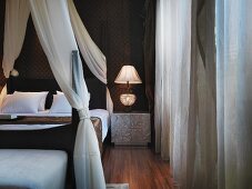 Elegant canopied bed with white curtains next to bedside table and retro lamp